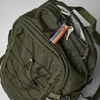 A close-up view of a green backpack with a rainbow-colored keychain and keys attached to an open zipper pocket. Náhľad obrázku produktu