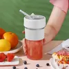 A person is holding a portable smoothie blender filled with a red smoothie, surrounded by fresh fruits like oranges, lemons, and strawberries, and some blueberries scattered on the table. Produktbild-Vorschau