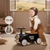 A baby dressed as a pilot is riding a retro black toy car indoors. Náhled obrázku produktu