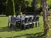 An outdoor dining set is arranged on a grassy lawn, surrounded by trees and foliage. Produktbild-Vorschau