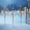 Three decorative LED light branches are placed in the snow next to a white picket fence during a snowfall. Produktbild-Vorschau