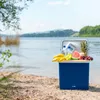 A blue cooler box filled with fruits and drinks sits on a sandy beach by a lake. Náhled obrázku produktu