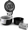 A black and gray air fryer with its lid open, showing the heating element and fan. The cooking basket and a rotisserie basket are placed next to it on a white background. Produktbild-Vorschau