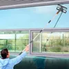 Person in blauem Kapuzenpullover, die einen langen Teleskop-Fensterreiniger an einem großen Außenfenster verwendet Voir les images du produit