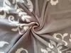 A close-up, swirled view of a grey fleece blanket with a white ornamental pattern. Produktbild-Vorschau
