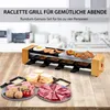 A raclette grill set with food items arranged around it on a wooden table. Produktbild-Vorschau