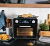 A kitchen counter scene featuring a black air fryer oven with a roasted chicken and bread rolls. Anteprima dell’immagine prodotto