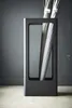 A modern, minimalist umbrella stand with umbrellas inside, set against a dark gray wall and a light gray floor. Produktbild-Vorschau