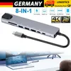 A USB-C hub adapter is shown connected to a laptop, with a larger screen in the background. Produktbild-Vorschau