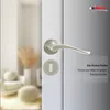A close-up of a silver door handle and lock mechanism on a white door, with a blurred background of a room interior. Produktbild-Vorschau