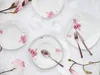 A table setting with floral-patterned porcelain plates and rose gold cutlery, decorated with magnolia branches. Náhľad obrázku produktu