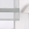 A close-up view of a sheer, light gray Roman blind with horizontal bands, partially covering a window. A pleated lampshade is visible on the right. Produktbild-Vorschau