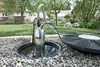 A submersible pump is shown in a garden pond, connected to a hose that leads to a large, flat disc-like object. Náhľad obrázku produktu