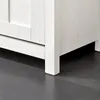 A close-up view of the bottom corner of a white wooden cabinet or shoe rack, showing its leg and the floor. Produktbild-Vorschau
