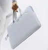 A person's hand holds a light gray laptop bag. Náhľad obrázku produktu