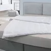 A white duvet is laid out on a bed with a grey headboard in the background. A grey ottoman and a dresser are visible in the background.