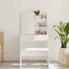 A white vanity table with a mirror and shelves filled with various bottles and containers, placed in a room with a plant and a bed frame visible. Náhled obrázku produktu
