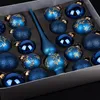 A box of blue Christmas ornaments with gold accents and a blue tree topper. Produktbild-Vorschau