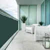 A balcony with a dark green privacy screen attached to the railing, white wicker furniture, and potted plants. Produktbild-Vorschau