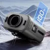 A grey portable fan with a blue digital display showing '100%' is positioned on a textured surface with a snowy mountain background. Produktbild-Vorschau