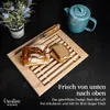 A bread cutting board with bread and a teapot on a dark surface. Produktbild-Vorschau