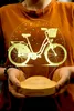 A person holds a 3D LED lamp shaped like a bicycle. Produktbild-Vorschau
