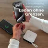 Hands charging two phones with a portable charger on a wooden table. Produktbild-Vorschau