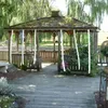 A wooden gazebo in a garden setting with decorative white ribbons hanging from the roof. Náhľad obrázku produktu