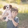 A young boy is holding a stuffed dog over his shoulder outdoors. Produktbild-Vorschau