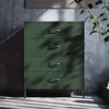 A green metal chest of drawers against a textured gray wall, with light casting shadows on the floor. Podgląd zdjęcia produktu