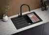 A black granite kitchen sink with a black faucet and a cutting board with cherry tomatoes is shown on a marble countertop. Produktbild-Vorschau