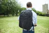 A person wearing a backpack stands in a grassy park with trees and a building in the background. Náhľad obrázku produktu