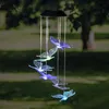 A solar-powered wind chime with butterfly-shaped lights hangs outdoors in a garden setting. Produktbild-Vorschau