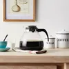 A coffee pot filled with coffee sits on a wooden table next to sugar and coffee containers, with a framed illustration on the wall behind it. Náhľad obrázku produktu