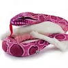 A pink python plush toy is coiled around white bone-like objects against a white background. Produktbild-Vorschau