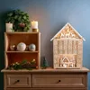 A wooden advent calendar shaped like a house, decorated with Christmas ornaments and lights, displayed on a wooden dresser. Náhled obrázku produktu