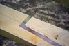 A close-up shot of a metal square ruler placed on a wooden beam. Anteprima dell’immagine prodotto