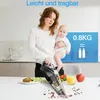A woman holds a baby while demonstrating a handheld vacuum cleaner in a kitchen setting. Produktbild-Vorschau
