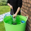 A person is using a submersible pump in a large green tub filled with water, next to a brick wall and a grassy area. Produktbild-Vorschau