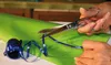 Hands are shown cutting blue ribbon with scissors on a roll of green wrapping paper. Náhled obrázku produktu