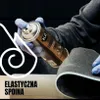 A hand wearing a blue glove holds a spray can over a piece of gray foam material. Náhled obrázku produktu