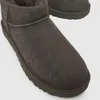 A close-up view of a pair of gray UGG boots with a dark green sole, set against a light gray background. Voir les images du produit