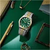 A Citizen watch is displayed on a green surface with other accessories like a pen, necklace, and a decorative frame. Voir les images du produit