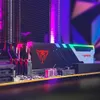 A close-up, low-angle shot of computer RAM modules with RGB lighting, set against a blurred background with purple and pink lighting. Podgląd zdjęcia produktu