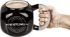 A hand holding a black kettlebell-shaped mug with text on it. Podgląd zdjęcia produktu