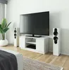 A white TV stand with a large black television on top, flanked by two white speakers. A potted plant is to the left, and a rug is in the foreground. Náhľad obrázku produktu