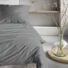 A neatly made bed with grey striped bedding and a vase with dried flowers in the background. Produktbild-Vorschau
