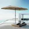 A large taupe double patio umbrella is set up on a wooden deck next to a swimming pool, with a modern white building in the background and the ocean beyond. Anteprima dell’immagine prodotto
