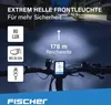 A bicycle handlebar with a headlight and display, illuminated by the headlight's beam on a street at night. Anteprima dell’immagine prodotto