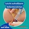 A close-up of a baby's diaper with a hand tearing the side seam, highlighting the "easy-tear" feature. The background is teal with marketing text and logos. Podgląd zdjęcia produktu